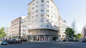 Ein mehrstöckiges Hotel mit geschwungener Fassade, zahlreichen Balkonen und einem Laden im Erdgeschoss mit dem Schild 'MODA'.
