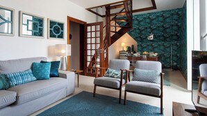 A living room with a grey sofa, two armchairs, a coffee table, and a staircase leading to a dining area.