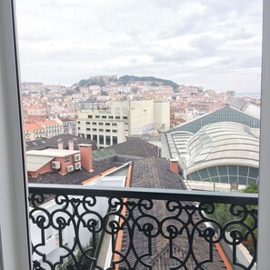 Udsigt over bybilledet fra en balkon med jerngitter, der viser en blanding af traditionelle og moderne bygninger, herunder en markant bygning med buet glas.