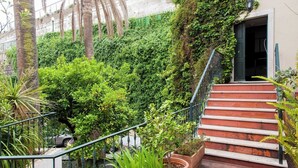 A staircase with a metal railing leading to a building entrance, surrounded by lush greenery and plants.
