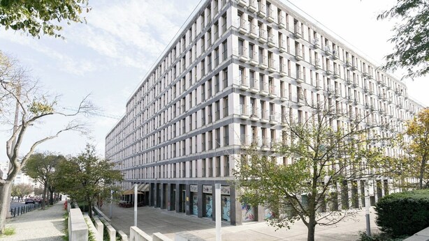 Een modern gebouw met een gevel in rasterstijl, meerdere balkons, een verharde stoep met bomen en een brandkraan.
