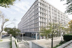 En modern byggnad med en fasad som har ett rutmönster, flera balkonger och en stenlagd trottoar med träd och en brandpost.