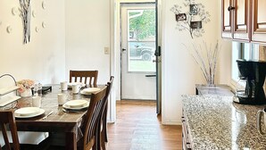 Zona pranzo con tavolo e sedie in legno, cucina con piani di lavoro in granito e una porta che dà sull'esterno.