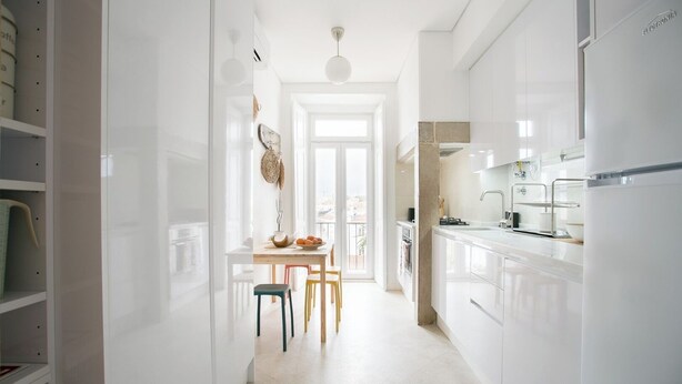 A bright, modern kitchen with white cabinets and a large refrigerator. There is a dining area with a table and chairs, and a view of the outside through a large window.