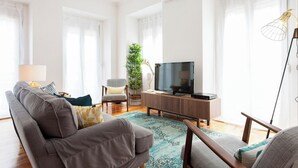 A modern living room with a grey sofa, a small armchair, a TV on a wooden stand, and a potted plant. - Principe Real beautiful 3 bedrs flat! Great WI-FI! (Lisboa)