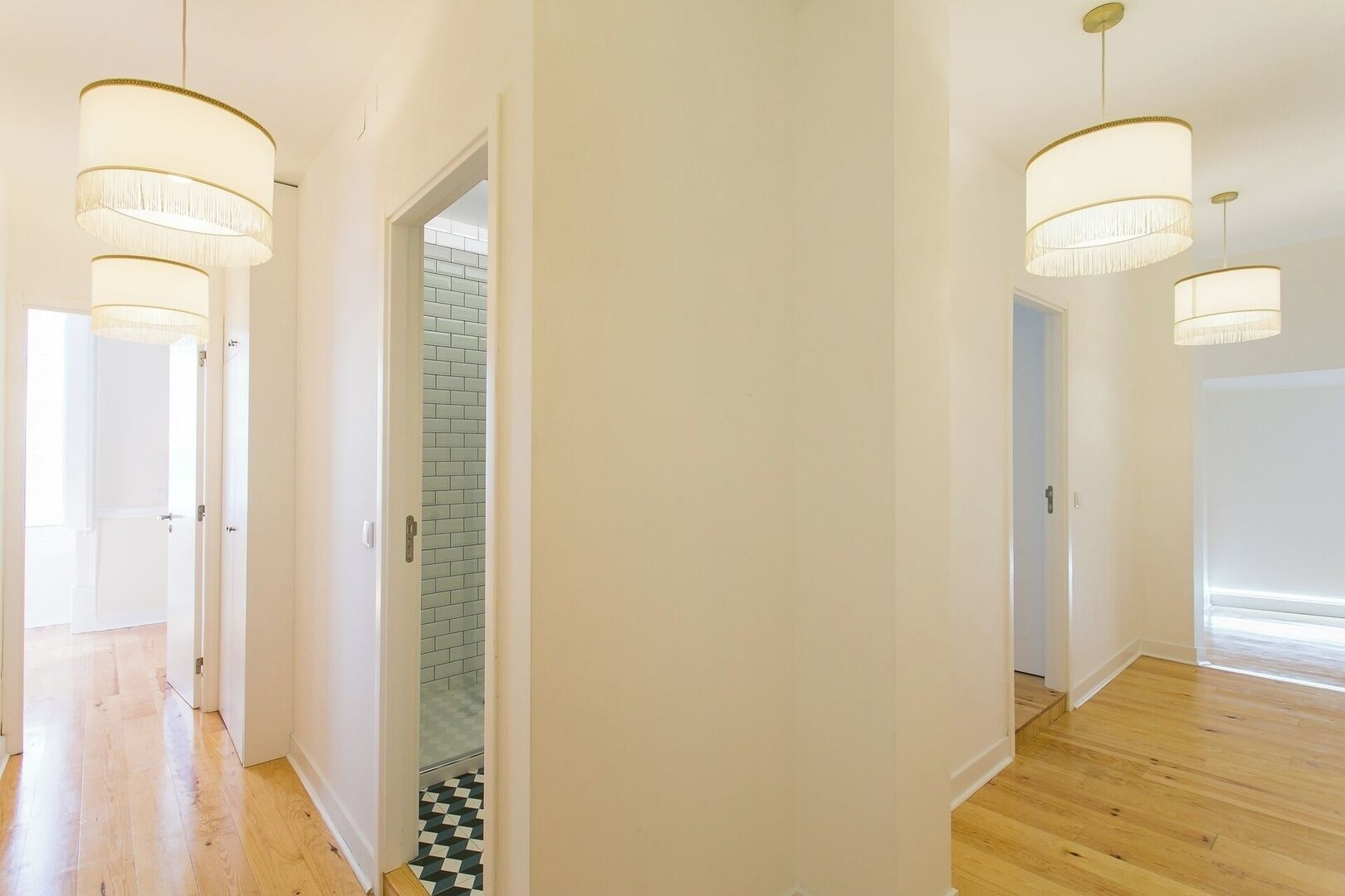 A hallway with wooden flooring, white walls, and two chandeliers.