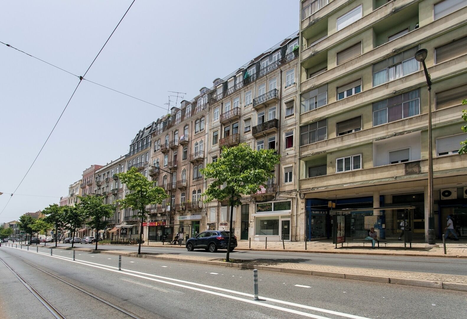Un edificio de varios pisos con balcones, una línea de tranvía y una acera para peatones.