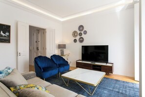 A living room with a sofa, two blue armchairs, a coffee table, a TV, and decorative plates on the wall. - Lisbon luxury retreat! 2 suites! (Lisboa)
