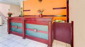 A reception desk with a floral arrangement, a coat rack, and a staircase in the background. - OYO 95023 Hotel Alamanda Garut (Garut)