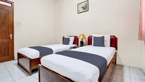 A hotel room with two single beds, a wooden door, a framed picture on the wall, and a lamp on the nightstand. - OYO 95023 Hotel Alamanda Garut (Garut)