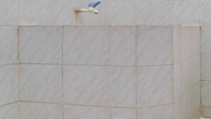 A corner of a room with white tiled walls and a corner sink with a blue faucet. - OYO 95023 Hotel Alamanda Garut (Garut)