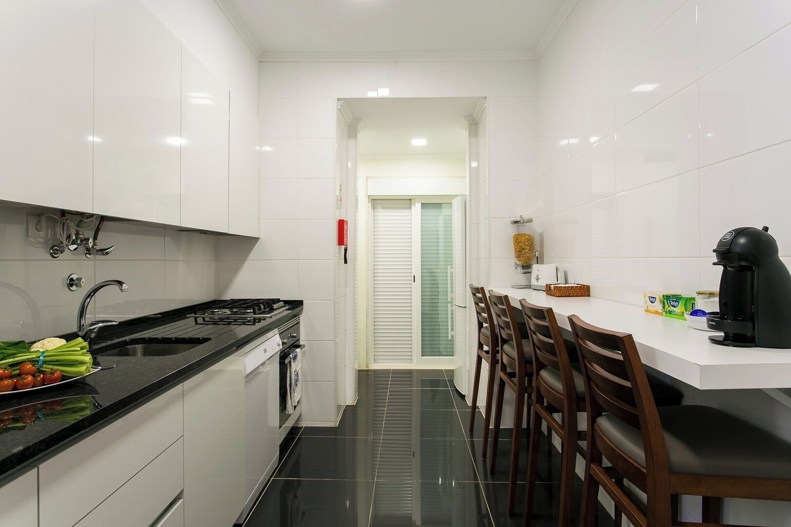 A modern kitchen with white cabinets, a black countertop, a gas stove, and a dining area with wooden chairs.