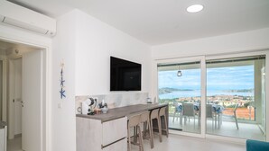 Een moderne keuken met een flatscreen televisie, een bar met krukken en een balkon met uitzicht op zee.