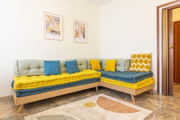 A modern living room with a sectional sofa, two framed artworks on the wall, and a patterned rug on the floor.