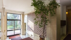 Un hall con un gran ventanal, un árbol en maceta y un papel tapiz estampado.