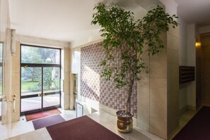 Un hall dâentrĂ©e dotĂ© dâune grande porte vitrĂ©e, dâun arbre en pot et dâun mur ornĂ© de motifs.