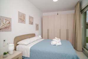 Un dormitorio con cama, mesita de noche, lámpara, planta en maceta y una obra de arte en la pared.