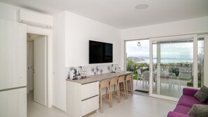Een moderne keuken met een flatscreen-tv, een eethoek met stoelen en een schuifdeur naar een balkon.