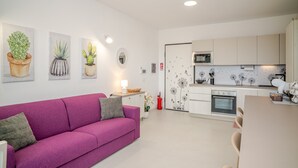 Een moderne woonkamer met een paarse bank, een keuken met witte kasten en kunstwerken aan de muren.