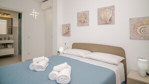 Een slaapkamer met een bed, handdoeken, kunstwerken, een nachtkastje en een bijzettafeltje.