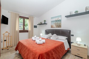 A neatly arranged bedroom with a bed, bedside tables, a TV, and a window with curtains. - Holiday Home 'New Attico Stella Maris Palau' with Sea View, Wi-Fi & Air Conditioning (Palau)