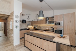 A modern kitchen with a central island, wooden cabinets, a black countertop, and stainless steel appliances. - Holiday Home 'New Attico Stella Maris Palau' with Sea View, Wi-Fi & Air Conditioning (Palau)
