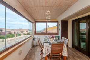 A balcony with a wooden ceiling, a table set for dining, and a view of the street. - Holiday Home 'New Attico Stella Maris Palau' with Sea View, Wi-Fi & Air Conditioning (Palau)