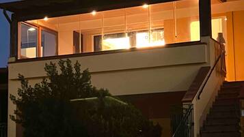 Ein zweigeschossiges Haus mit einer sichtbaren Treppe, einer Steinmauer und einem geparkten Auto davor.