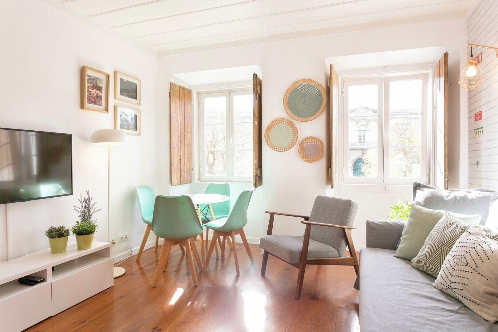 Een moderne woonkamer met een televisie, een eettafel met stoelen, een bank en decoratieve objecten aan de muur.