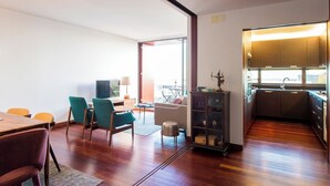 Ein modernes Wohnzimmer mit Holzboden, einem Essbereich mit Tisch und Stühlen, einer Couch und einer kleinen Küchenzeile mit Spüle und Schränken.