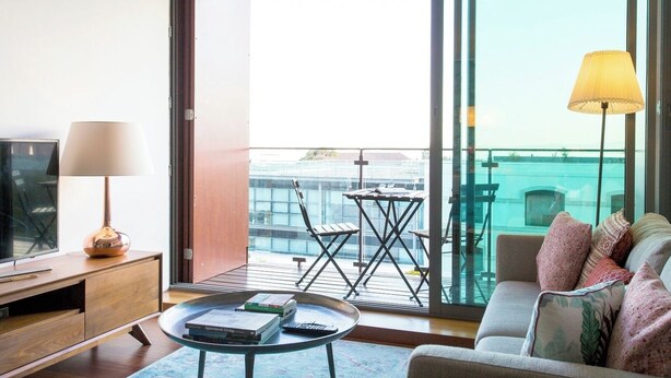 Ein modernes Wohnzimmer mit einer Couch, einem Couchtisch, einem Fernseher und einem Balkon mit Tisch und Stühlen.