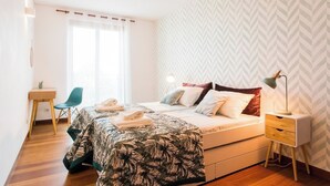 Ein Schlafzimmer mit Bett, Nachttisch, Lampe, Stuhl und Schreibtisch mit Pflanze.