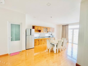 A modern kitchen with wooden cabinets, a stainless steel refrigerator, and a dining area with a table and chairs. - EMERALD APARTMENTS (ho chi minh)