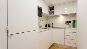 Cozinha compacta com armários brancos, pia de aço inoxidável e piso de madeira.