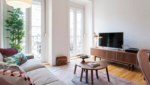 Uma sala de estar moderna com um sofá, uma mesa de centro, uma TV e uma janela grande.