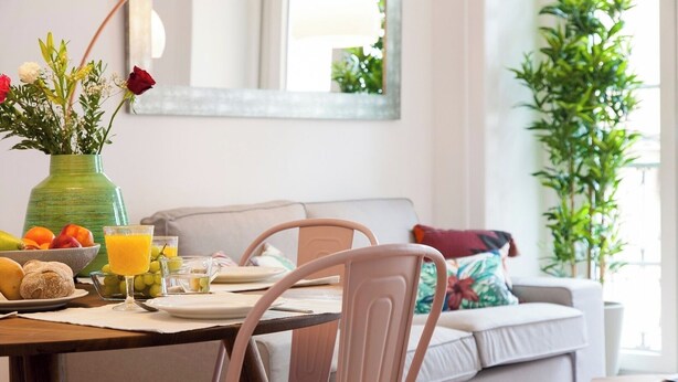 Uma área de refeições com uma mesa posta para o café da manhã, incluindo frutas, um copo de suco de laranja e um vaso com flores.