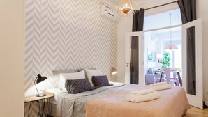 Quarto moderno com cama, luminária de cabeceira e vista para uma área de refeições ao ar livre.