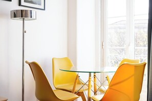 A room with a glass table and four yellow chairs, a floor lamp, and a window with a view of trees. - Lisbon great 1 bdr flat with air condicioner! (Lisboa)
