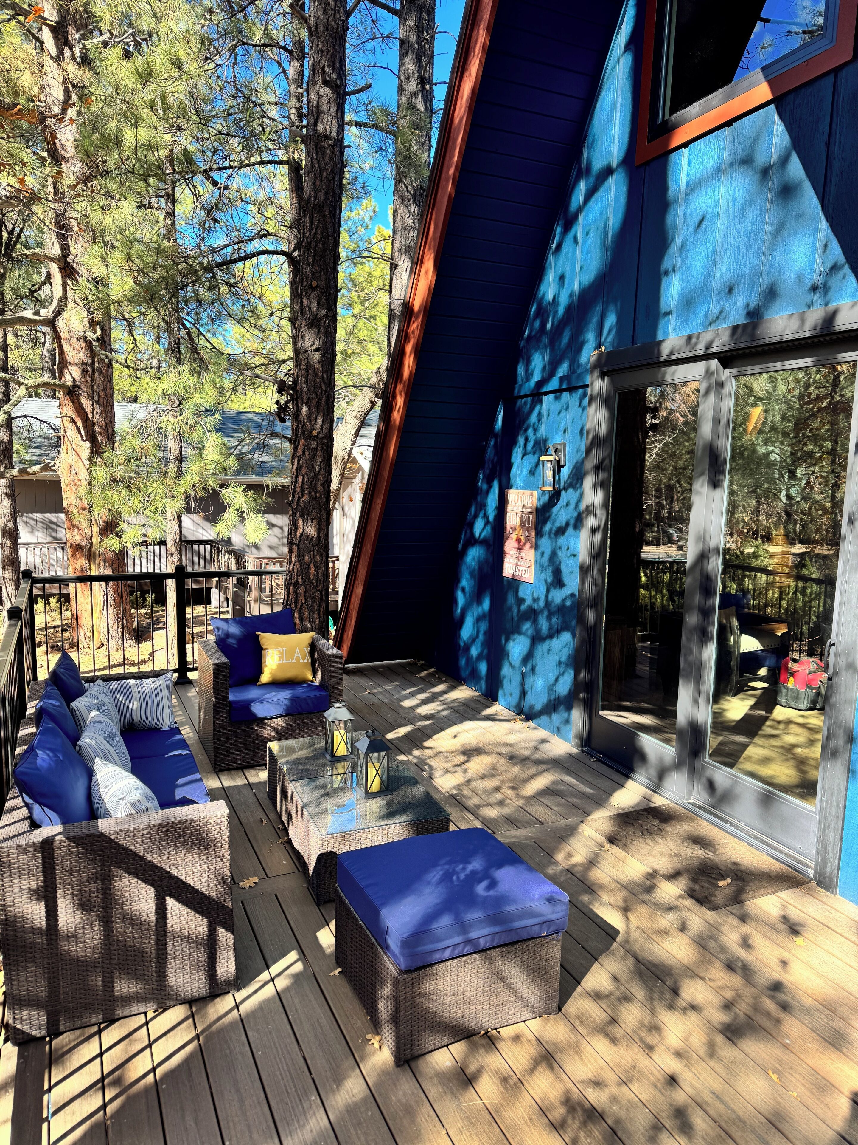 Une terrasse dotée de meubles en osier et de coussins, entourée d’arbres.