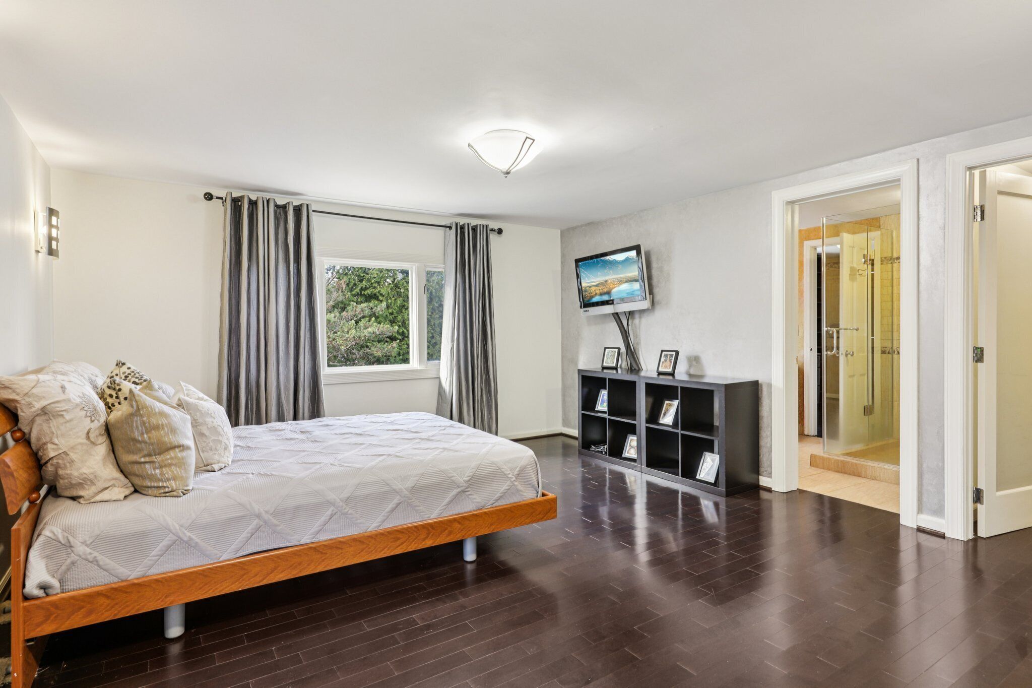Une chambre à coucher comprenant un lit, un téléviseur, une console sur laquelle sont posés des cadres photos, et une porte donnant sur une salle de bain.