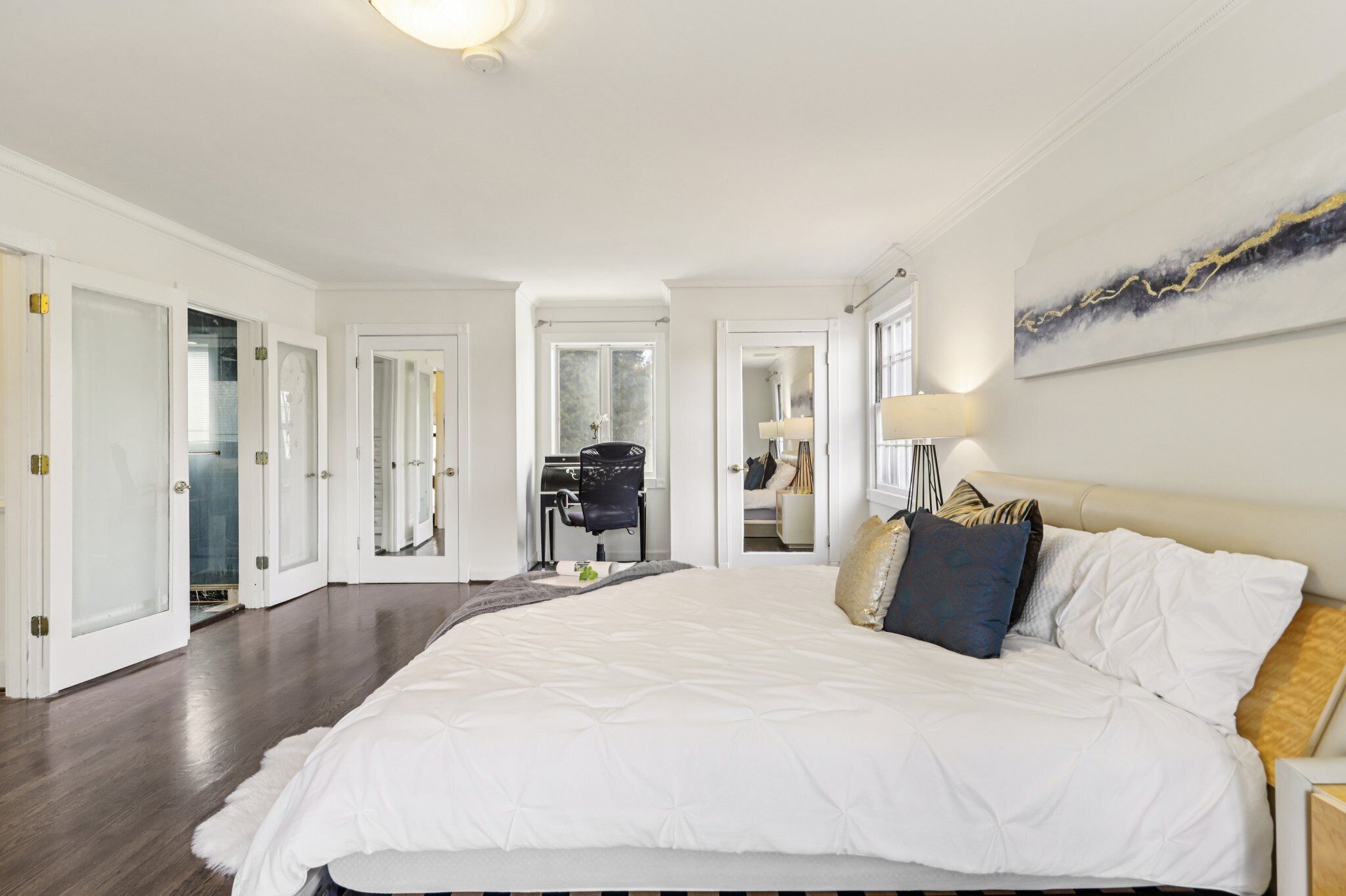A spacious bedroom with a large bed, a desk, and a chair. There are multiple doors leading to other rooms.