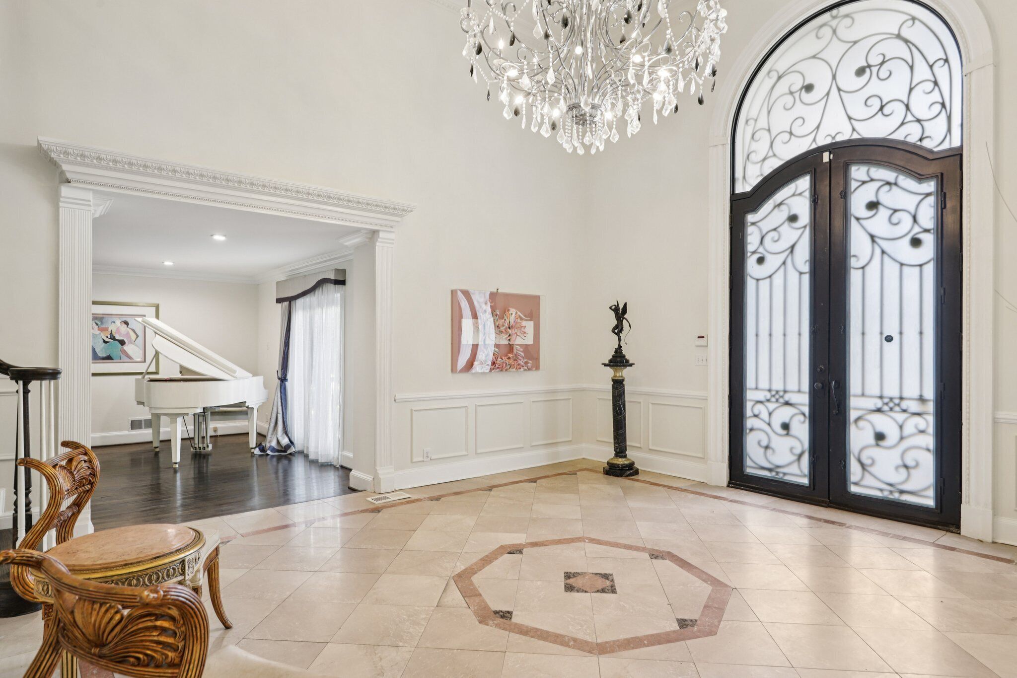 Un hall d’entrée spacieux agrémenté d’un grand piano, d’un lustre et d’une porte décorative.