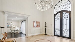 Un hallo espacioso con un piano de cola, una araña de cristal y una puerta decorativa.