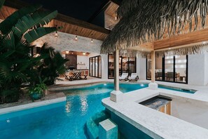 A pool area with a thatched roof structure, lounge chairs, and a dining area with a table and chairs. - Luxe Home Short Walk to Beach (Potrero)