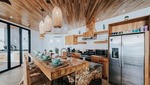 Une cuisine moderne dotée d’un îlot central, de meubles en bois, d’appareils électroménagers en acier inoxydable et de luminaires suspendus.