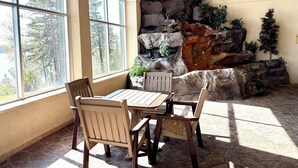 A sunlit room with a large window, a wooden table, and chairs, a rock wall with plants, and a stone floor. - NEWLY LISTED Lakeside 2 Queen Fireplace Studio~Pool/Hot tub/Sauna (Two Harbors)