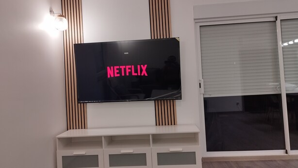 Una sala de estar moderna con un televisor de pantalla plana montado en la pared, una puerta corrediza de vidrio y un mueble de entretenimiento blanco pequeño debajo.