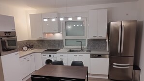 Una cocina moderna con gabinetes blancos, un refrigerador de acero inoxidable, horno empotrado, lavadora y un comedor con dos sillas.
