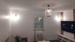 Una sala de estar moderna con un sofá, un sillón, una mesa de centro, un televisor y una ventana con persianas.