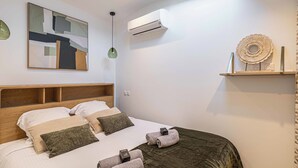 A modern bedroom with a skylight, a bed with multiple pillows, a bedside table, an air conditioning unit, and a decorative shelf. - Warm apartment near Palais Festivals and old port (Cannes)